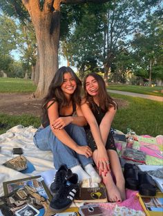 two young women sitting on a blanket in the park with their feet crossed and smiling