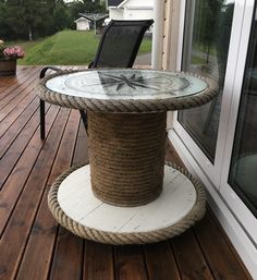 a round table with rope and glass top sitting on a deck next to a window