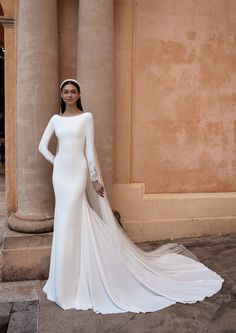 a woman in a white wedding dress standing next to pillars with her hands on her hips