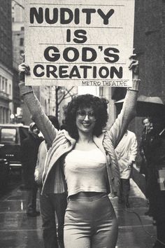 a woman holding up a sign that says nudity is god's creation