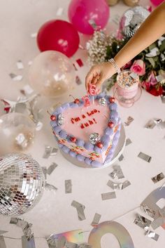 a heart shaped cake on a table surrounded by confetti and balloons