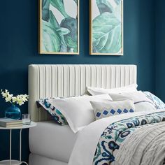 a bedroom with blue walls, white bedding and two framed pictures above the bed