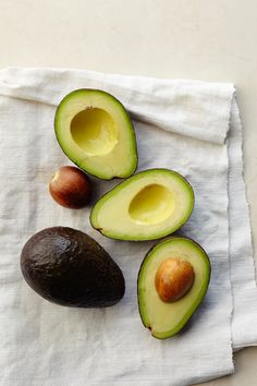 an avocado cut in half sitting on top of a white towel next to two other fruits