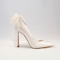 a white high heeled shoe with a bow on the front and side, against a gray background