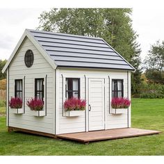 a small white shed with two windows and flower boxes on the roof