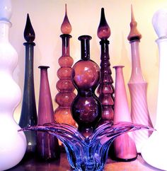 many different colored vases on a table with white and pink walls behind them in the background