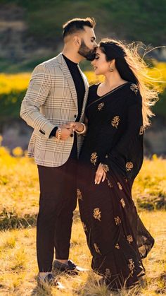 a man and woman standing next to each other in a field with yellow flowers on the grass