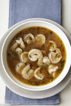 a white bowl filled with soup and shrimp on top of a blue napkin next to a spoon