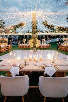 a table set up for a wedding with candles on it and lights strung from the ceiling