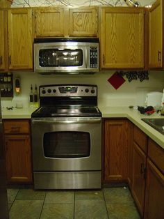 a stainless steel stove and microwave in a kitchen with wooden cabinets, tile flooring and white counter tops