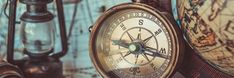 an old fashioned compass sitting on top of a table next to other antique lamps and lanterns