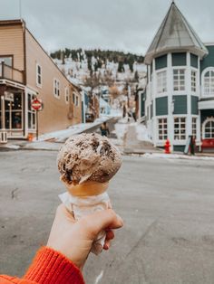 a person holding an ice cream cone in front of a street with buildings on both sides