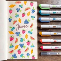 an open notebook with fruit and berries on it, surrounded by markers that read june