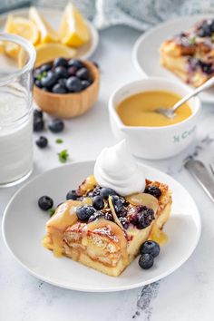 a white plate topped with blueberry cheesecake next to bowls of lemonade and whipped cream