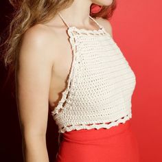 a woman with long hair wearing a white crochet halter top and red skirt