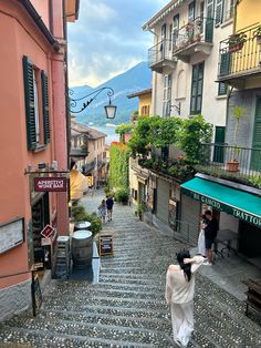 a woman walking down a cobblestone street in an old town with shops and restaurants