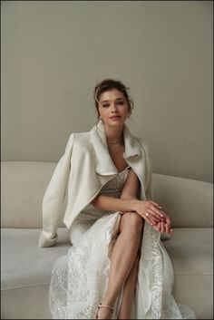 a woman sitting on top of a couch in a white dress and jacket with her legs crossed