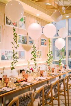 a long table is set up for a party with white balloons and greenery on the wall