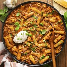 a skillet filled with pasta, meat and cheese on top of a wooden table