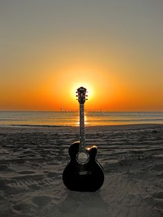 an acoustic guitar sitting on the beach at sunset