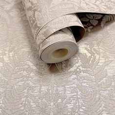 a roll of paper on top of a white wallpaper with an intricate floral design