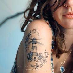 a woman with a lighthouse tattoo on her arm and behind her is a blue background