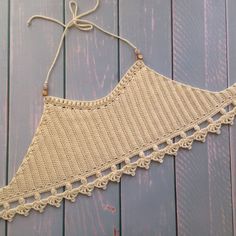 a crocheted triangle is hanging from a string on a wooden surface with wood planks