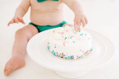 a baby sitting in front of a white cake with sprinkles on it