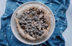 a small pizza covered in powdered sugar on top of a white plate next to a blue towel