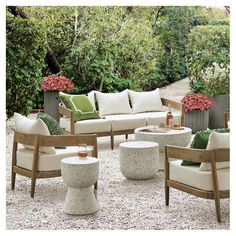 an outdoor seating area with white cushions and green pillows on the couches, surrounded by greenery