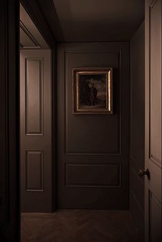 an empty hallway with a framed painting on the wall and wooden floors in front of it