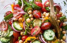 a glass bowl filled with cucumber, tomatoes and chickpeas salad on top of a marble counter