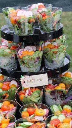 a table topped with lots of plastic cups filled with salads and veggies