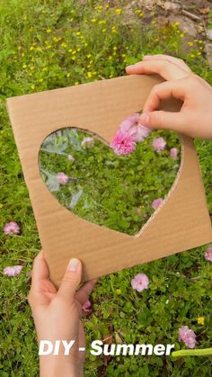 someone is making a heart shaped mirror out of cardboard and some flowers in the grass