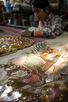 a woman is sitting at a table with several plates on it and there are many different designs on the cloth