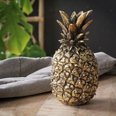 a gold pineapple sitting on top of a wooden table next to a pillow and potted plant