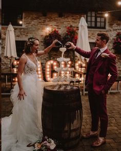 a man and woman standing next to each other in front of a barrel with wine glasses on it