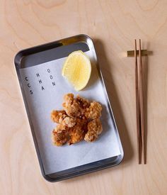 a tray with chopsticks, lemon and chicken on it next to some chop sticks