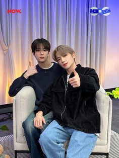 two young men sitting on top of a white couch in front of a blue curtain