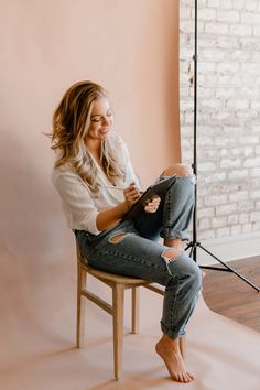 a woman sitting on a chair in front of a brick wall with her legs crossed