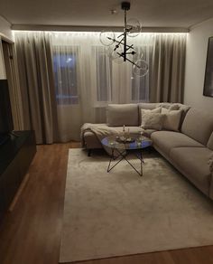 a living room filled with furniture and a chandelier hanging from the ceiling in front of a window