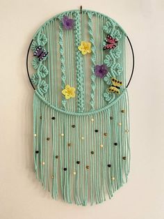 a crocheted dream catcher with flowers and beads hanging on the wall in front of a white wall