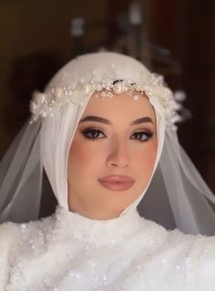 a woman wearing a white veil with pearls on the head and neck, is looking at the camera