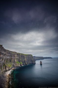 the cliffs are very high on the water and dark clouds hover over them in the distance