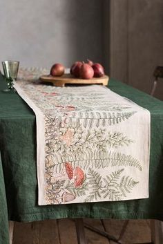 a green table cloth with flowers and leaves on it next to a bowl of apples