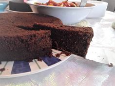 a chocolate cake sitting on top of a white plate next to a bowl of fruit