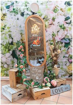 a mirror sitting on top of a wooden box next to flowers and other items in front of a wall