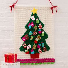 a crocheted christmas tree hanging on a wall next to a red box and white brick wall