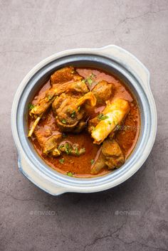 a bowl filled with chicken curry on top of a gray countertop next to a spoon