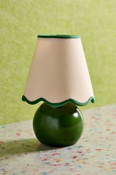 a green lamp with a white shade on it sitting on a table next to a wall